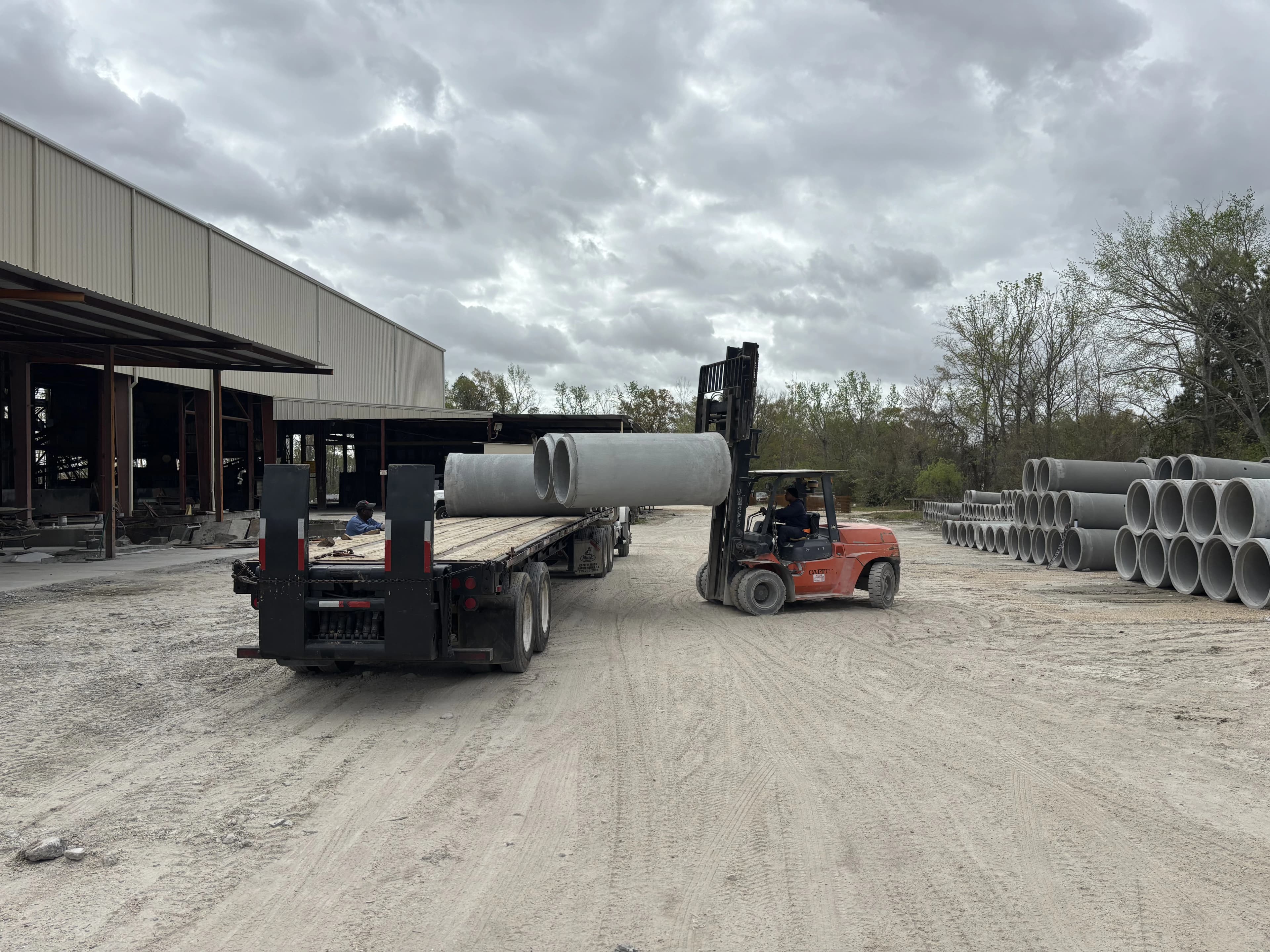 Worker loading round pipe with forklift on to Semi Trailer truck on the yard