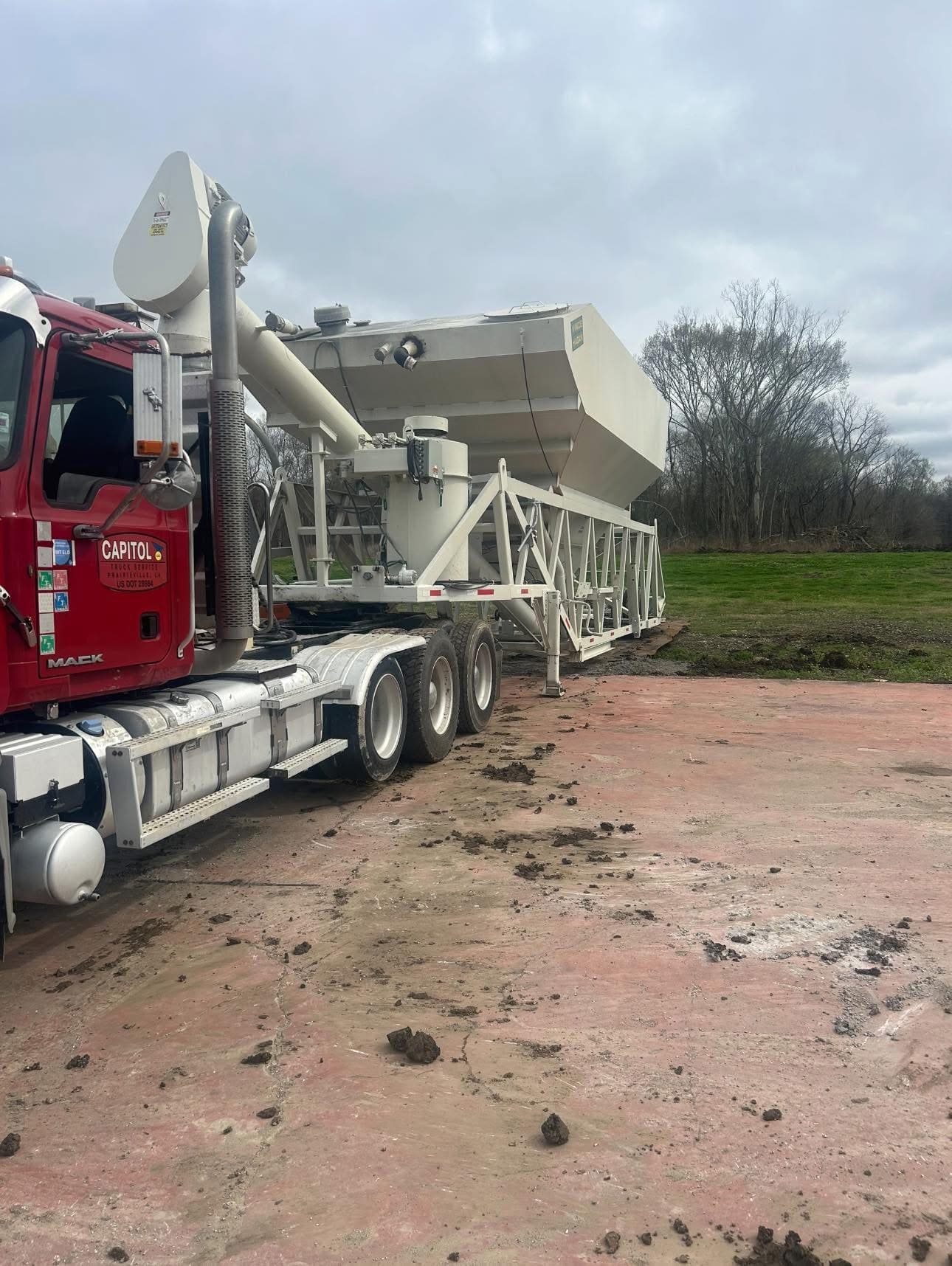 Semi Trailer truck dumping dirt on to open field on cloudy day
