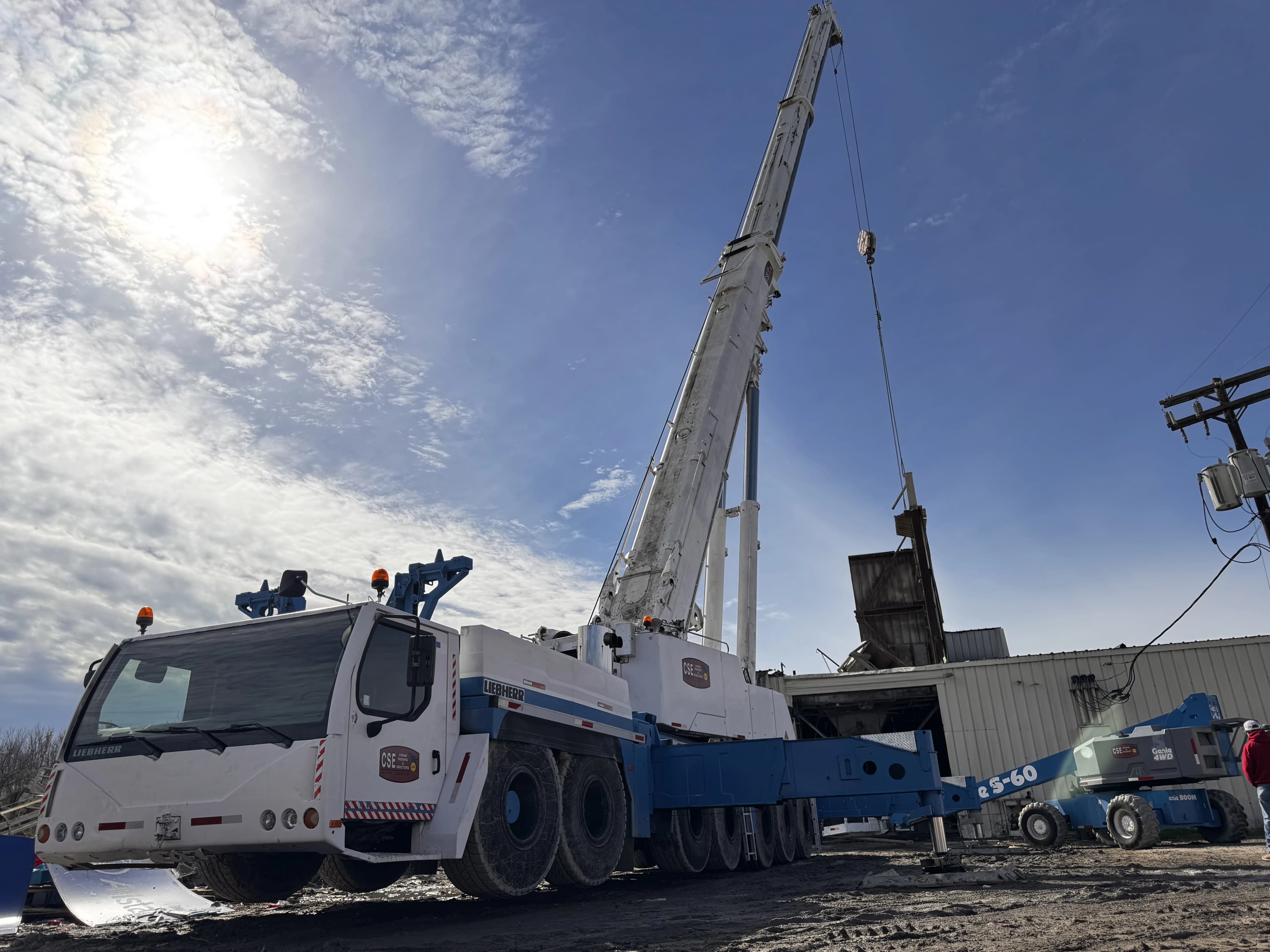 Crane truck fully erected on yard with boom truck behind it on sunny day