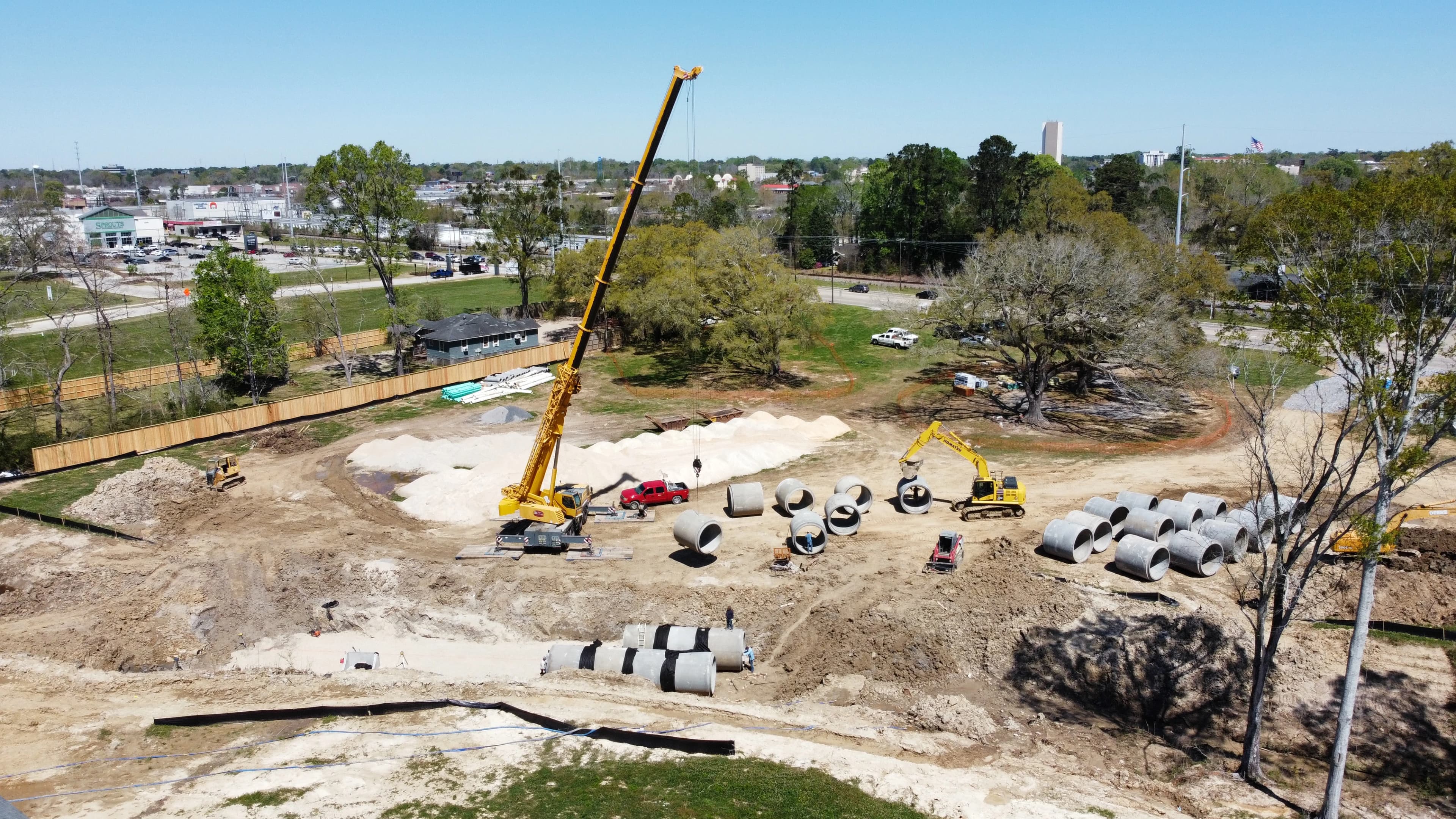 Crane erected on job site moving round pipe near excavated hole on sunny day