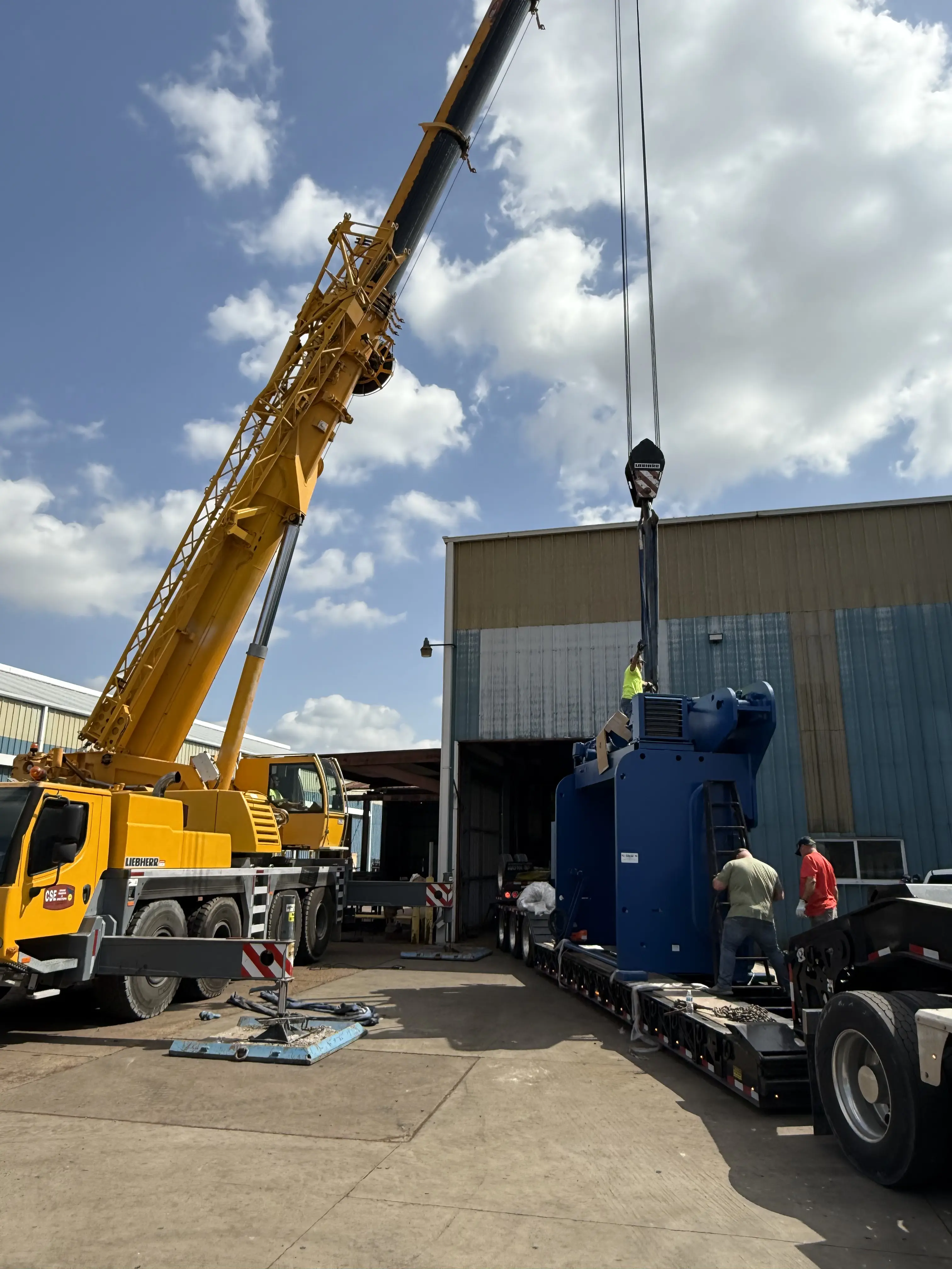 Crane moving large blue object outside on a bright day